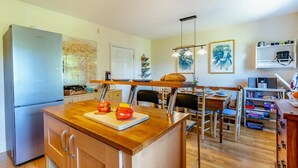 A modern kitchen with a central island, wooden cabinets, a refrigerator, and a dining area with chairs and a table. - 3 Bed in Hawes (oc-ds967) (Hawes)