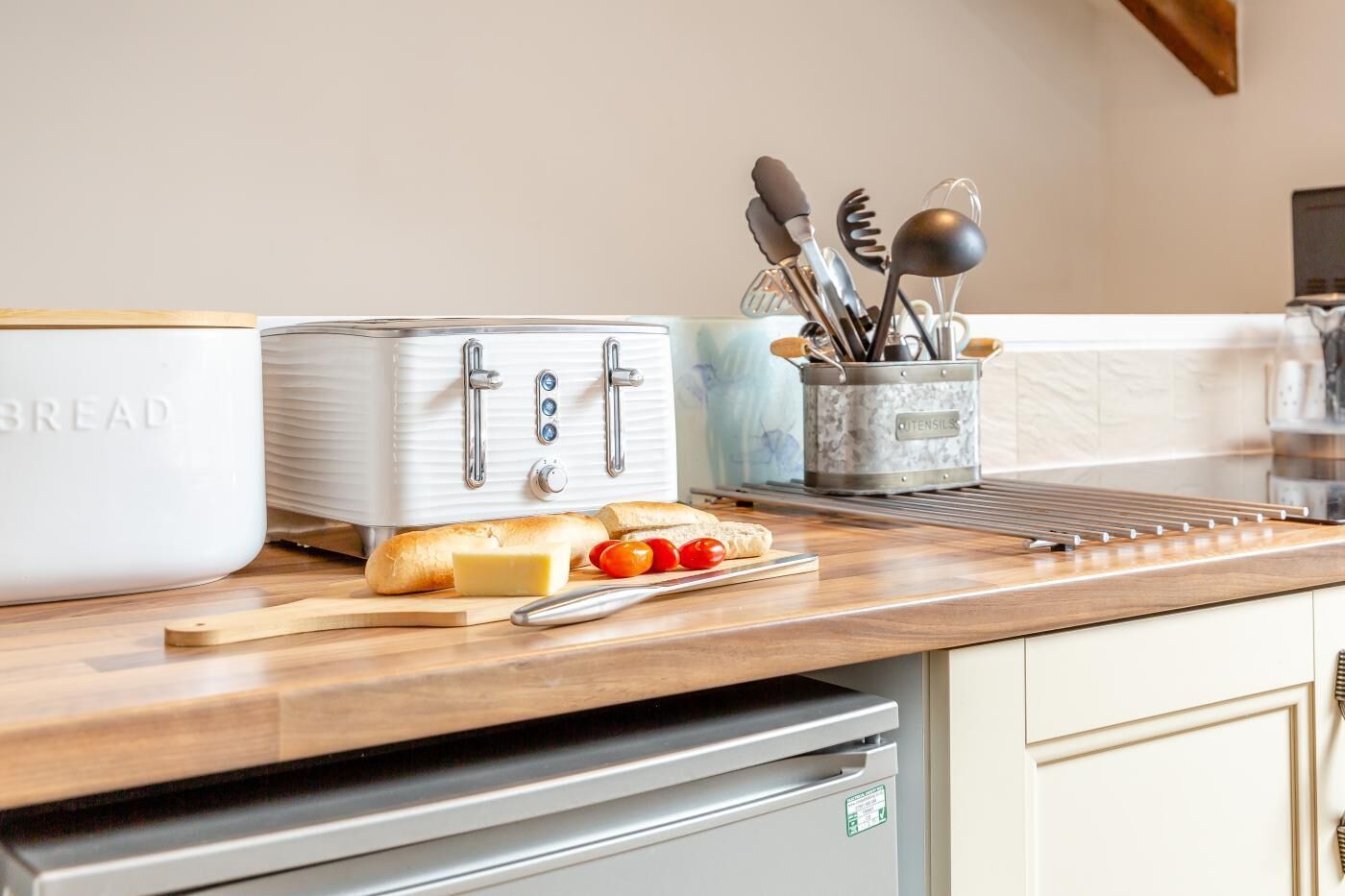A kitchen with a vintage toaster, a bread box, a cutting board with bread and tomatoes, and a utensil holder.