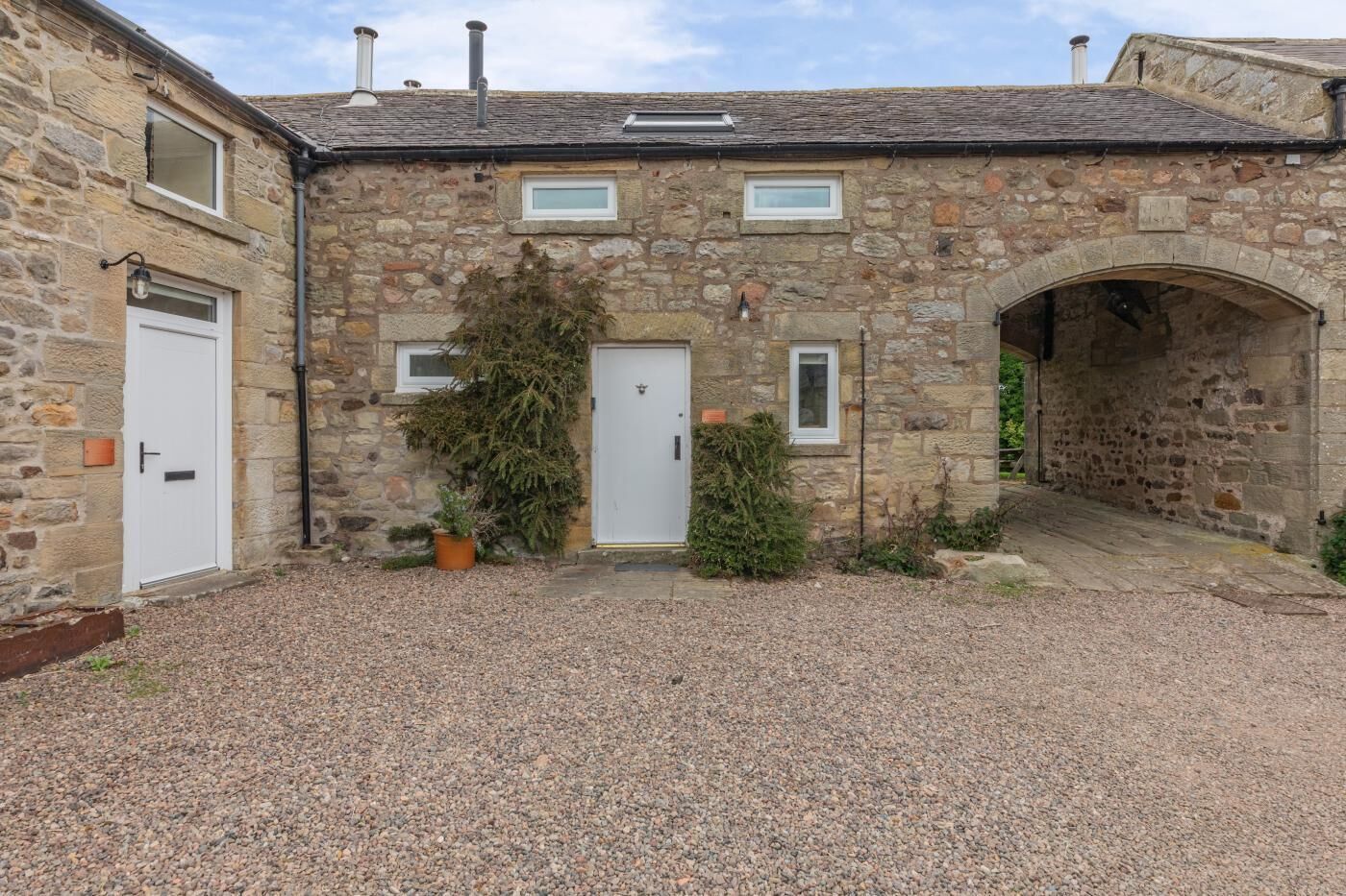 A stone building with a gravel courtyard, two doors, and a small archway.