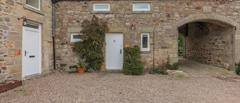 A stone building with a gravel courtyard, two doors, and a small archway.