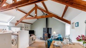 Um apartamento acolhedor no estilo loft, com vigas de madeira expostas, cozinha equipada com eletrodomésticos modernos, área de jantar com mesa posta para dois e sala de estar com lareira.