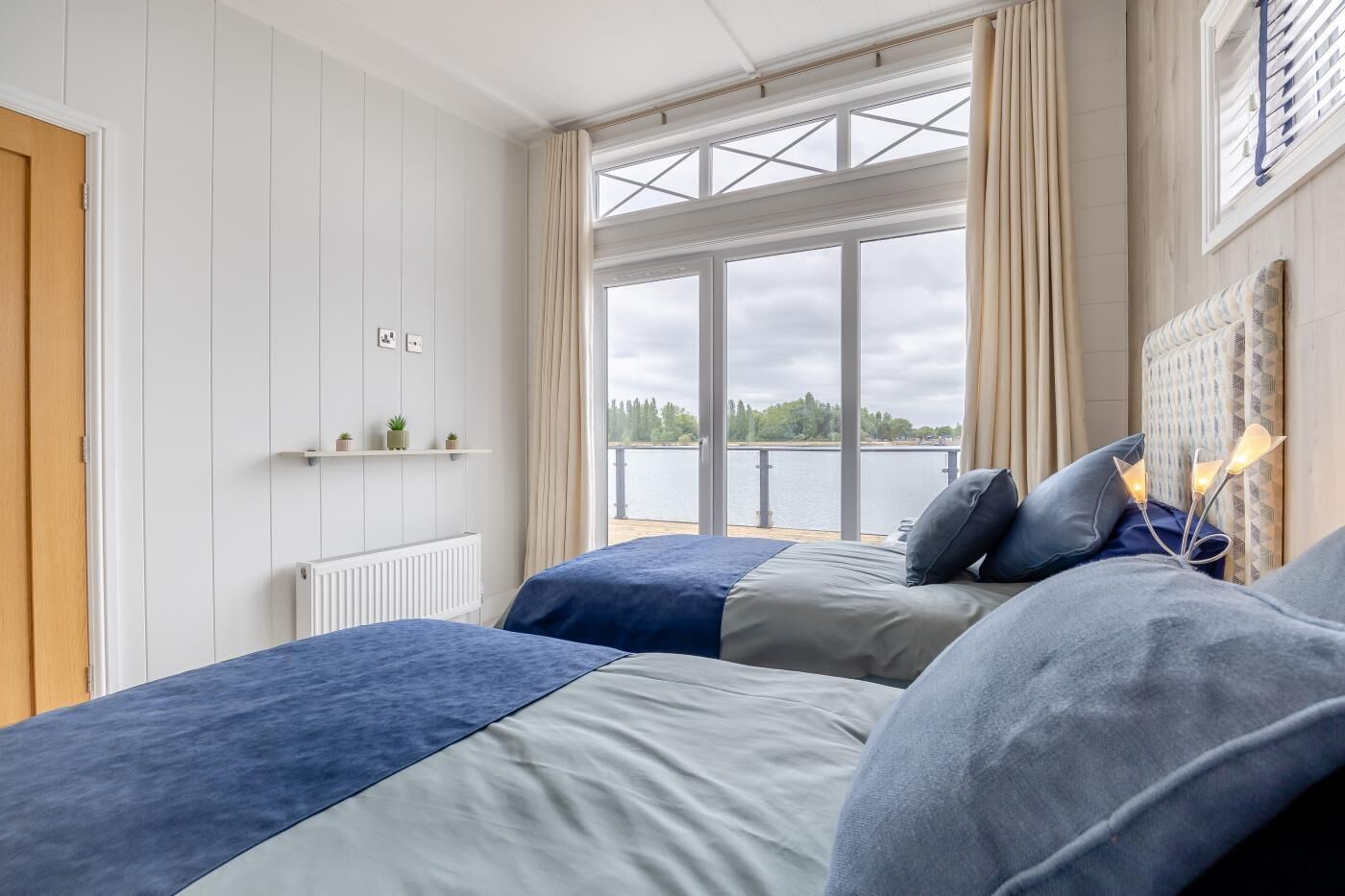 A bedroom with two beds, a window with a view of a lake, and a radiator.