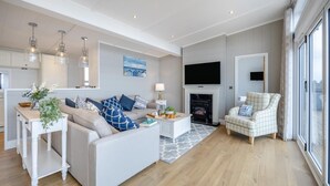 A modern living room with a sofa, armchair, and coffee table, a fireplace, and a TV mounted on the wall. - 2 Bed in Tallington (oc-b32208) (Maxey)