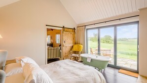 A bedroom with a bed, a chair, a bathtub, and a sliding door leading to a balcony with a view of the countryside. - 1 Bed in Wickhambrook (oc-tosh) (Wickhambrook)