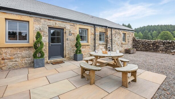 A stone building with a tiled patio and a round wooden table with benches. - 2 Bed in Gilsland (oc-t32230) (Waterhead)