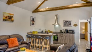 A modern living room with a sofa, coffee table, and bar stools. A kitchen with a stove, microwave, and sink is visible. - 2 Bed in Gilsland (oc-t32230) (Waterhead)