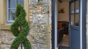 A stone exterior with a door leading to a living area with a sofa and a painting. - 2 Bed in Gilsland (oc-t32230) (Waterhead)