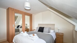 Un dormitorio con cama, mesitas de noche, espejo y lámpara de techo.