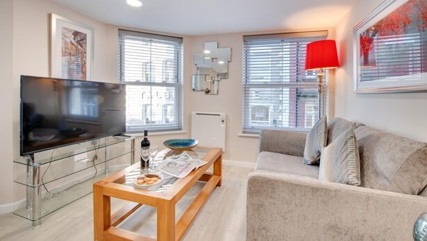 A living room with a TV, sofa, coffee table, and a red lamp. - 1 Bed in Whitby (oc-w503) (Whitby)