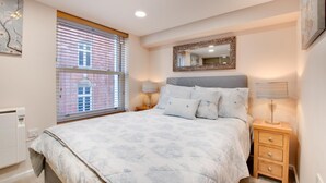 A bedroom with a bed, bedside tables, a mirror, and a window with blinds. - 1 Bed in Whitby (oc-w503) (Whitby)