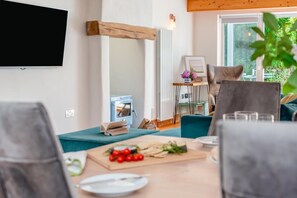 Ein modernes Wohnzimmer mit einem Holzbalken, einem Flachbildfernseher, einem kleinen Tisch mit einem Buch und einem Essbereich mit einem Tisch für zwei Personen.