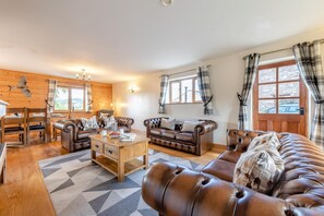A cozy living room with a wooden floor, a leather sofa, a coffee table, and a dining area with a wooden table and chairs. - 9 Bed in Brecon (oc-cvelo) (Crai)