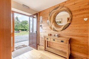 Un intérieur en bois avec une porte donnant sur l’extérieur, une console avec des tiroirs et un miroir décoratif accroché au mur.