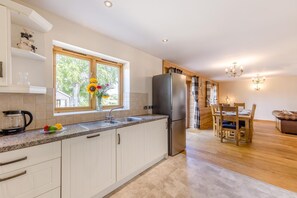 A modern kitchen with a large window, a refrigerator, and a dining area with a wooden table and chairs. - 9 Bed in Brecon (oc-cvelo) (Crai)