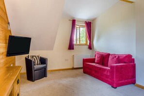 A room with a black leather chair, a red velvet sofa, a television mounted on a wooden wall, a window with curtains, and a radiator. - 9 Bed in Brecon (oc-cvelo) (Crai)