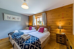 A double bed with patterned bedding, a bedside table with a lamp, and a window with curtains. - 9 Bed in Brecon (oc-cvelo) (Crai)