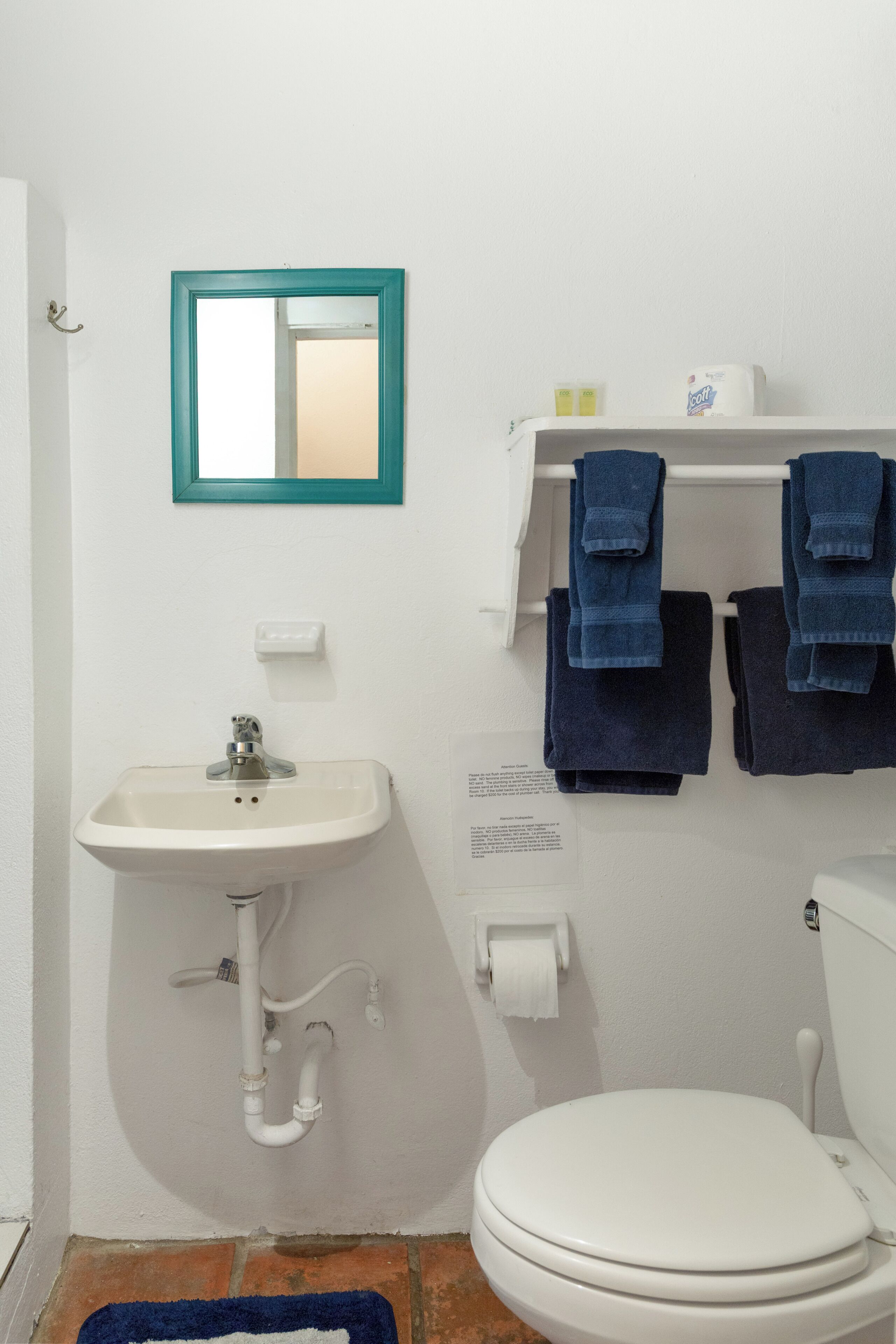 Ein Badezimmer mit einem weißen Waschbecken, einem Spiegel mit blaugrünem Rahmen, einer Toilette und zwei Handtüchern, die an einem Wäscheständer hängen.