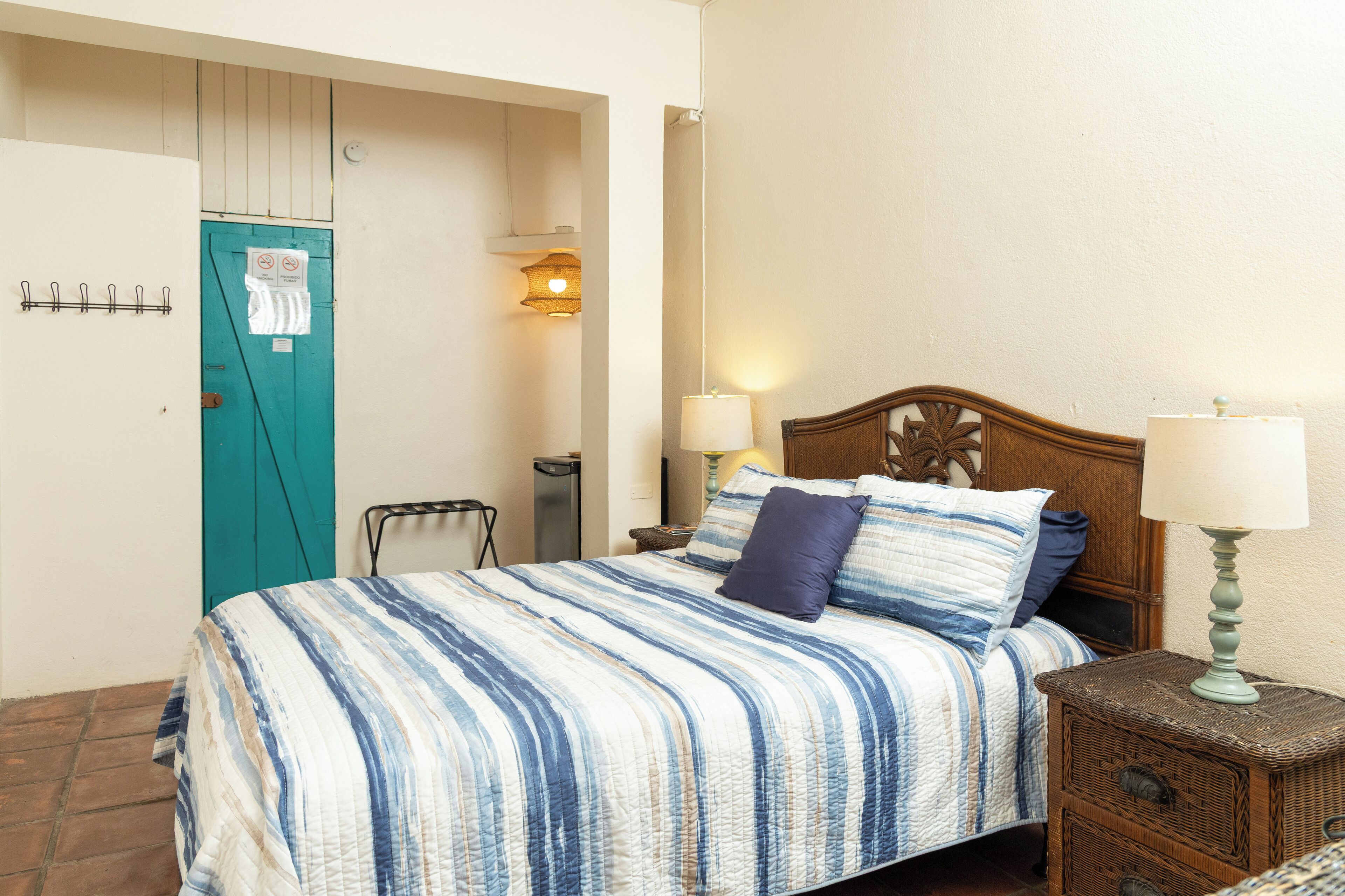 A bedroom with a bed, bedside lamps, a wooden headboard, a nightstand, and a door with a sign.