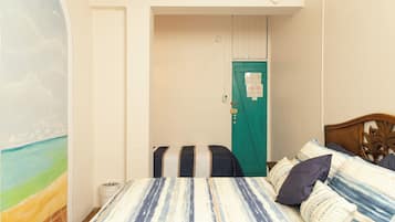 A bedroom with a bed, a green door, a wall with a painting, and a small trash bin.