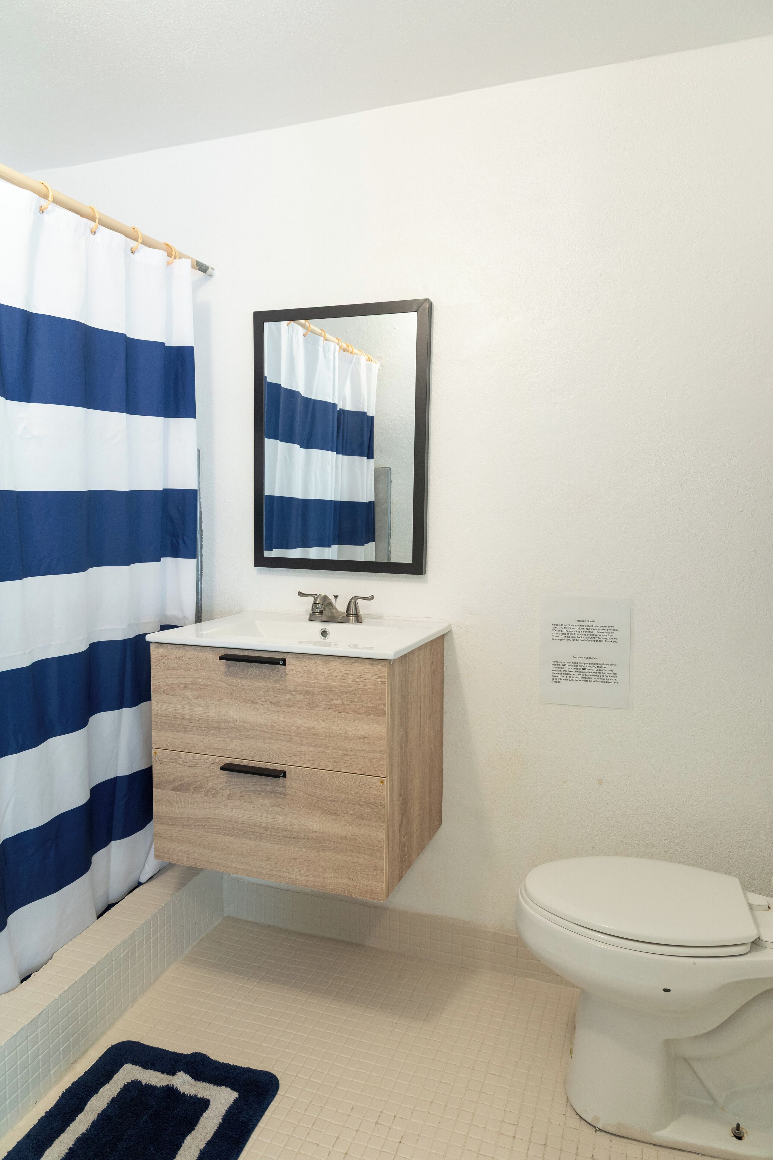 A bathroom with a white sink, wooden vanity, a mirror, a white toilet, and a blue and white striped shower curtain.