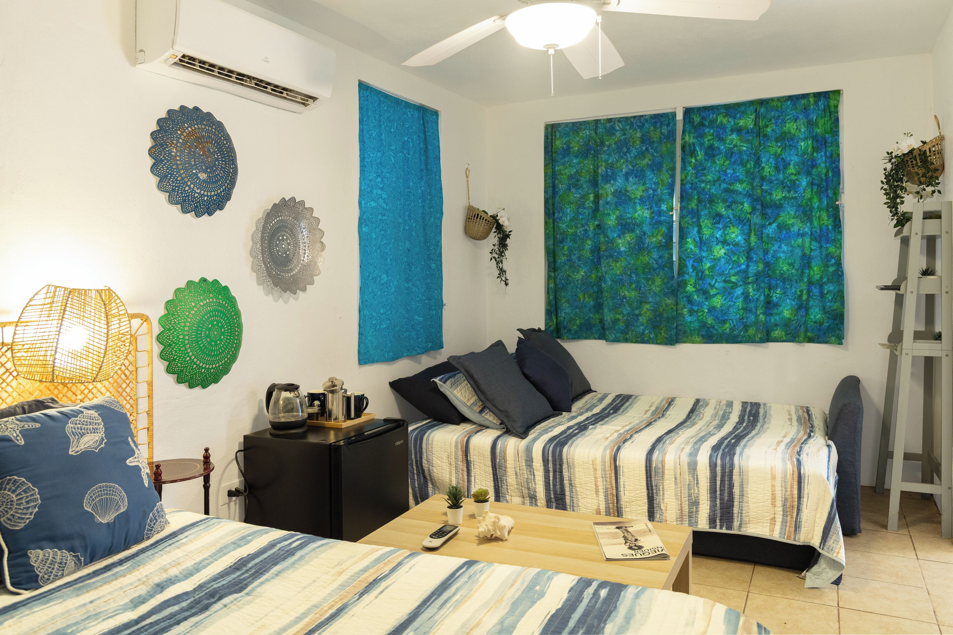 A room with two beds, a small table, a ceiling fan, and decorative wall art.