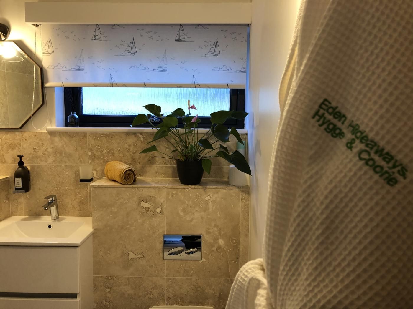 Een badkamer met een wastafel, handdoek, een plant in pot en een raam met een bootontwerp.
