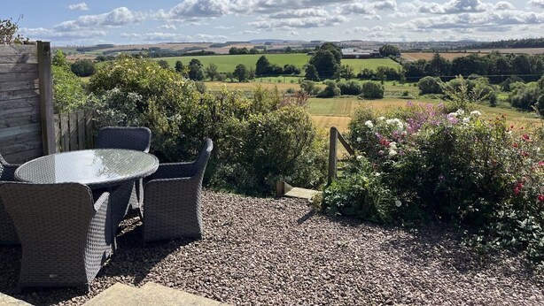 Un espace extérieur aménagé avec des meubles en osier et offrant une vue sur un paysage rural.