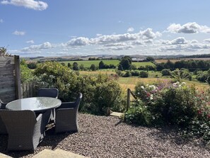 Un espace extérieur aménagé avec des meubles en osier et offrant une vue sur un paysage rural.