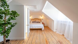 Une chambre avec un plafond en pente, un lit avec une literie blanche, une table de chevet, une lampe et une plante en pot.