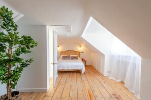 Ein Schlafzimmer mit schrägem Dach, einem Bett mit weißer Bettwäsche, einem Nachttisch, einer Lampe und einer Topfpflanze.