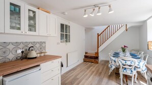 Une cuisine spacieuse avec des meubles blancs, un plan de travail en bois et un coin repas avec une table dressée pour quatre personnes.