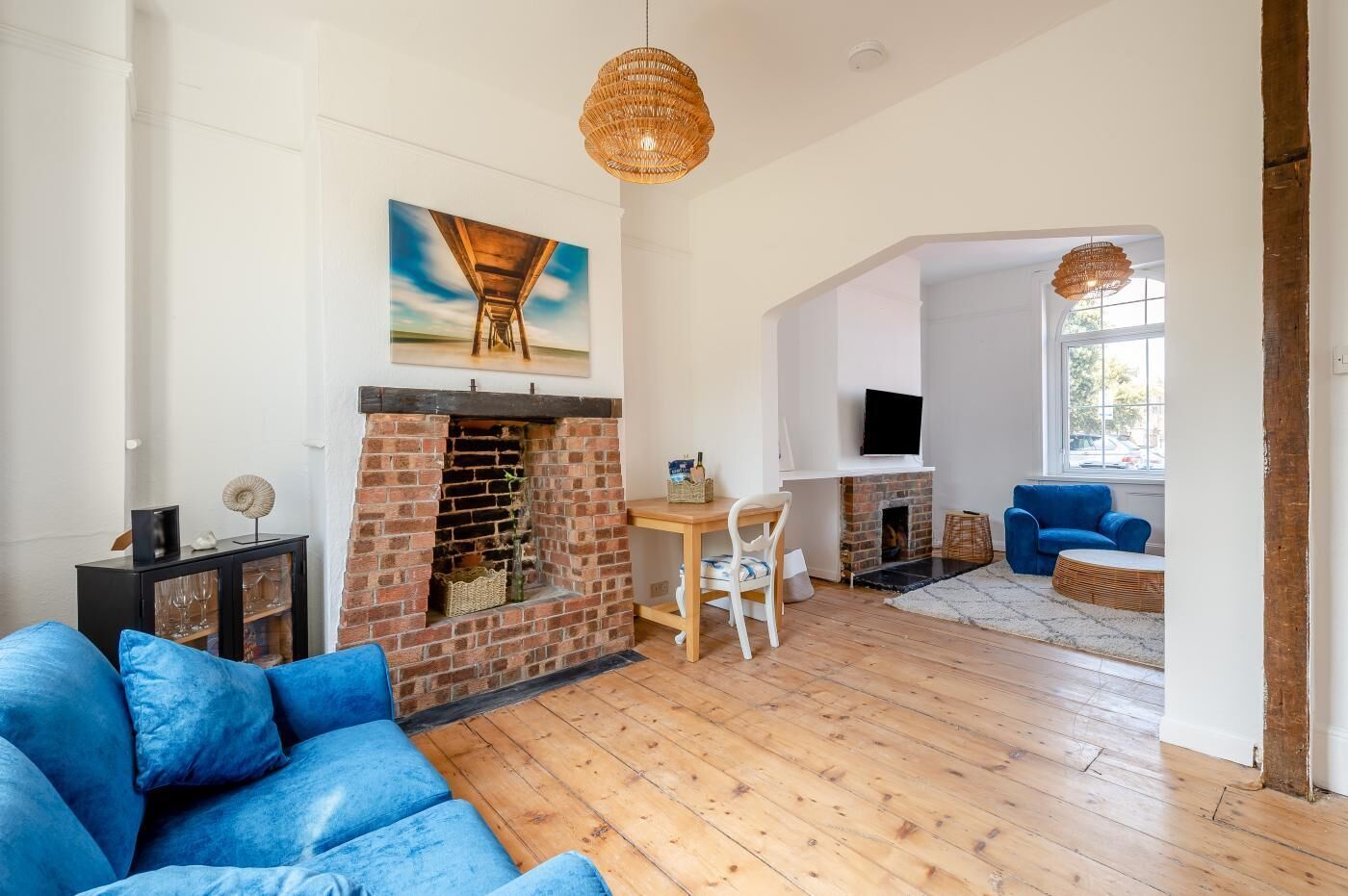 A living room with a brick fireplace, a blue sofa, a dining table with chairs, and a television mounted on the wall.