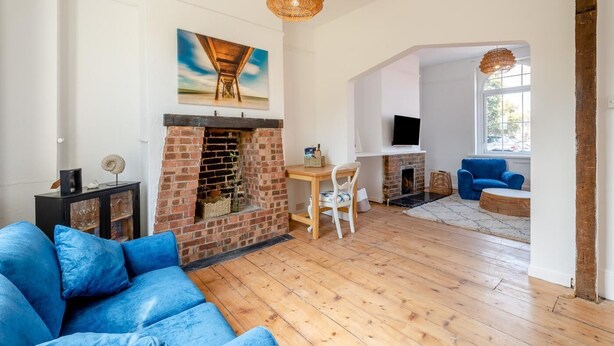 Un salon avec une cheminée en briques, un canapé bleu, une table à manger avec des chaises et un téléviseur fixé au mur.