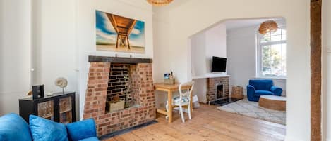 A living room with a brick fireplace, a blue sofa, a dining table with chairs, and a television mounted on the wall.