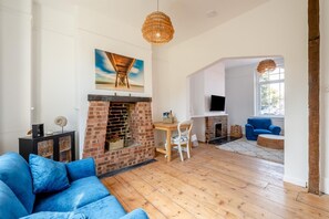 A living room with a brick fireplace, a blue sofa, a dining table with chairs, and a television mounted on the wall. - 4 Bed in Deal (oc-t32219) (Deal)