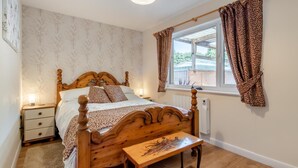 A bedroom with a wooden bed, bedside tables, a nightstand, a window with patterned curtains, and a view of the outside. - 1 Bed in Apley (oc-l32084) (Apley)