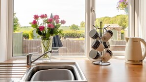 A kitchen with a sink, a vase of pink flowers, a mug rack, and a pitcher on the counter. - 1 Bed in Apley (oc-l32084) (Apley)