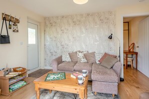A cozy living room with a sofa, a coffee table with a board game, and a door leading to another room.