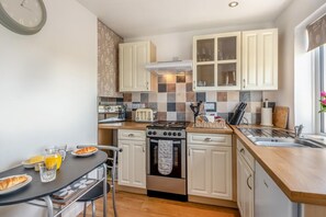 A compact kitchen with white cabinets, a gas stove, a built-in oven, a sink, and a dining area with a table and chairs.