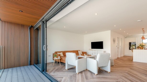 Ein modernes Wohnzimmer mit Sofa, Couchtisch und Sesseln. Ein Fernseher ist an der Wand montiert und im Hintergrund ist eine Küche erkennbar.