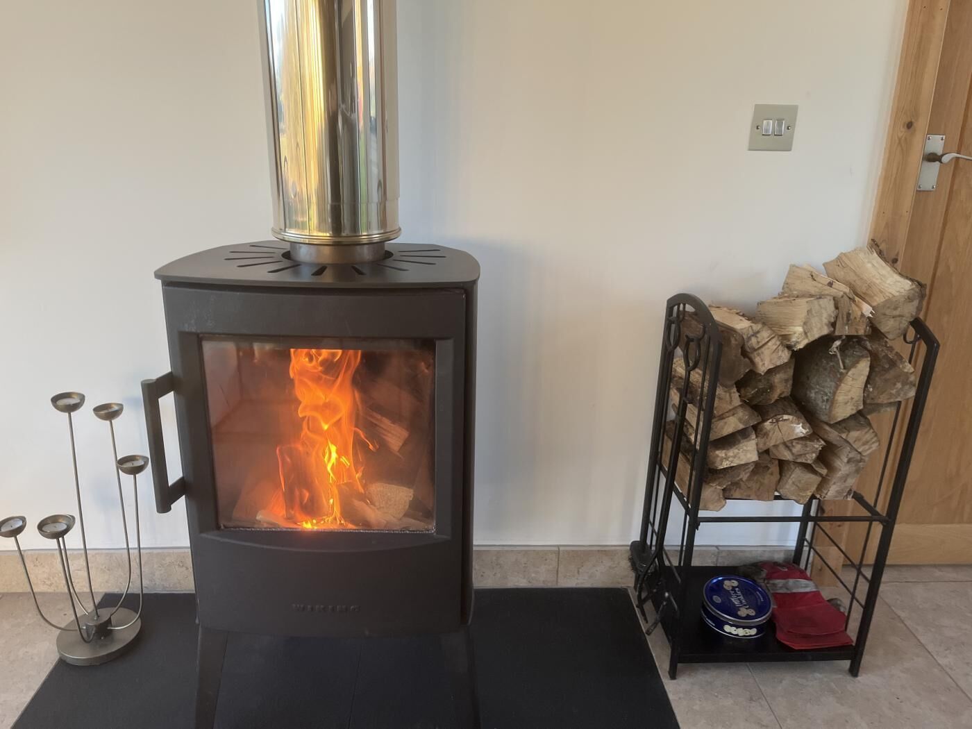 A wood-burning stove with a glass front, a metal chimney, and a black mat in front.