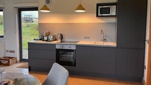 Une cuisine moderne avec des meubles gris, un four encastré, un micro-ondes et des luminaires suspendus.