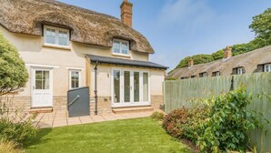 Ein Haus mit Strohdach, Wintergarten und einem gepflegten Garten.