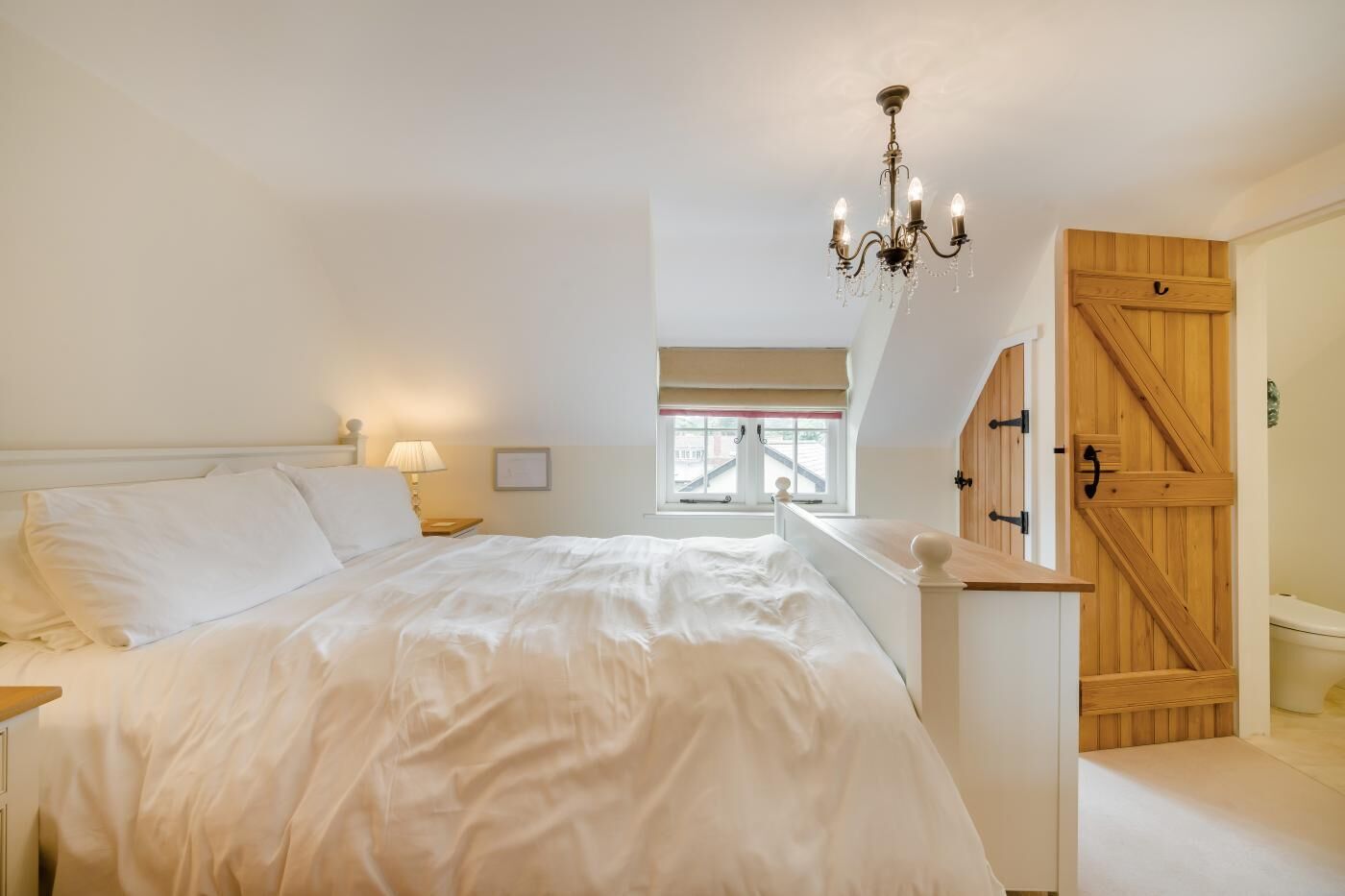 Une chambre avec un grand lit, un lustre, une armoire en bois et une fenêtre donnant sur un beau paysage.