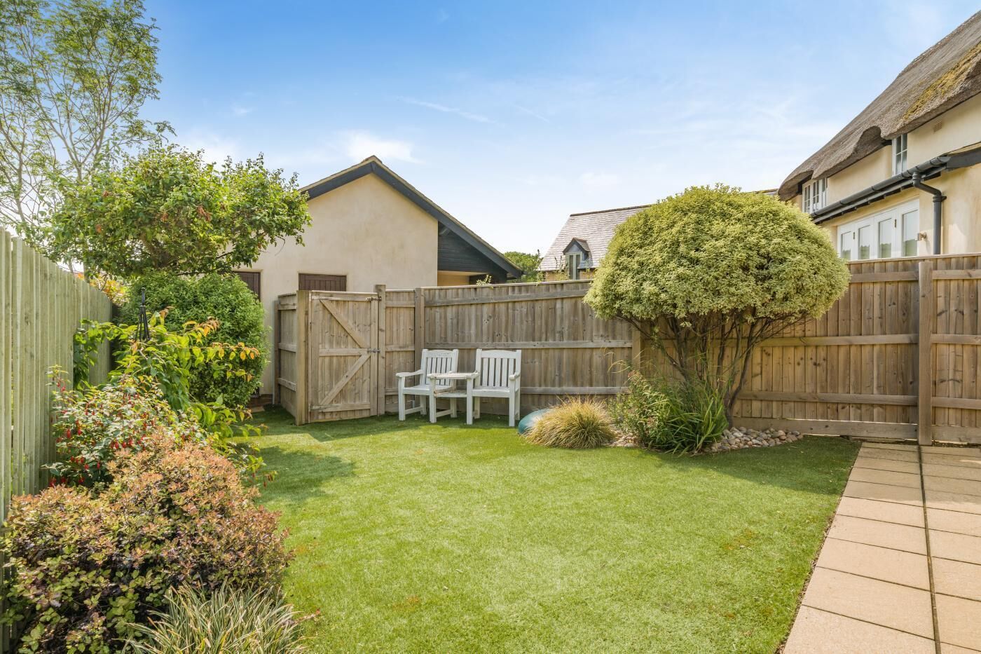 A backyard with a wooden fence, a small tree, and two white chairs.