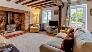 A cozy living room with exposed wooden beams, a brick fireplace, a comfortable sofa, a television, and a bookshelf. - 4 Bed in Sudbourne (oc-w32267) (Sudbourne)