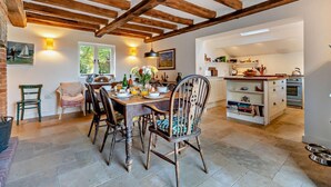 A dining area with wooden beams, a kitchen with white cabinets, and a dining table set for four. - 4 Bed in Sudbourne (oc-w32267) (Sudbourne)