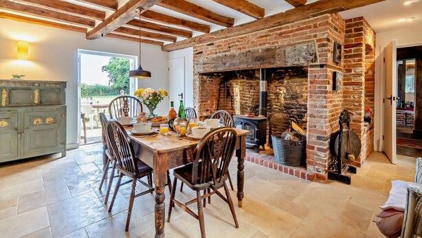 A rustic dining area with exposed wooden beams, a brick fireplace, and a table set for breakfast. - 4 Bed in Sudbourne (oc-w32267) (Sudbourne)
