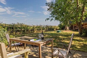 A wooden table with a bottle of wine and a glass, set outdoors with a view of a vineyard and a wooden fence in the background. - 2 Bed in Sudbourne (oc-w32264) (Sudbourne)