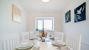 A dining room with a white table set for four, white chairs, and a window with a view. - 3 Bed in Leswalt (oc-g32241) (Leswalt)